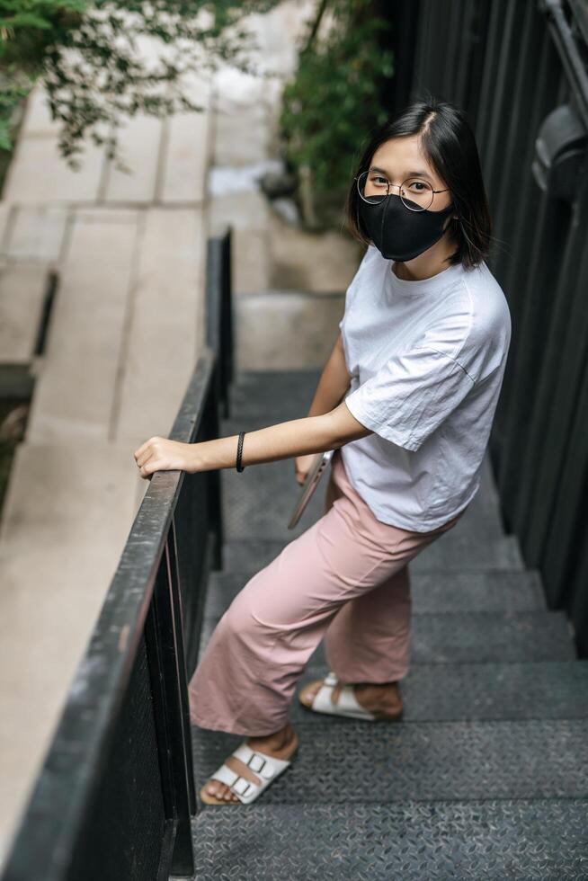 donna che indossa una maschera, tiene in mano un laptop e in piedi sulle scale. foto