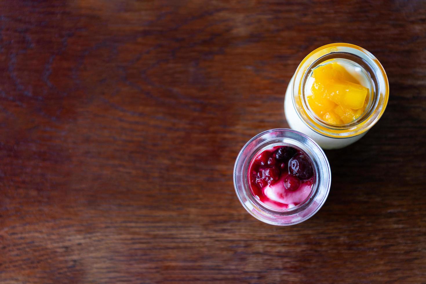 Yogurt greco con frutti di bosco e mango in vasetti di vetro su sfondo di legno foto