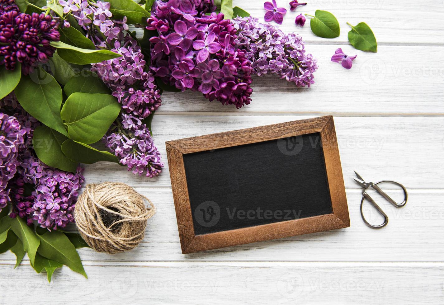 cornice di fiori lilla freschi su sfondo di legno con spazio copia sulla lavagna, composizione floreale piatta foto