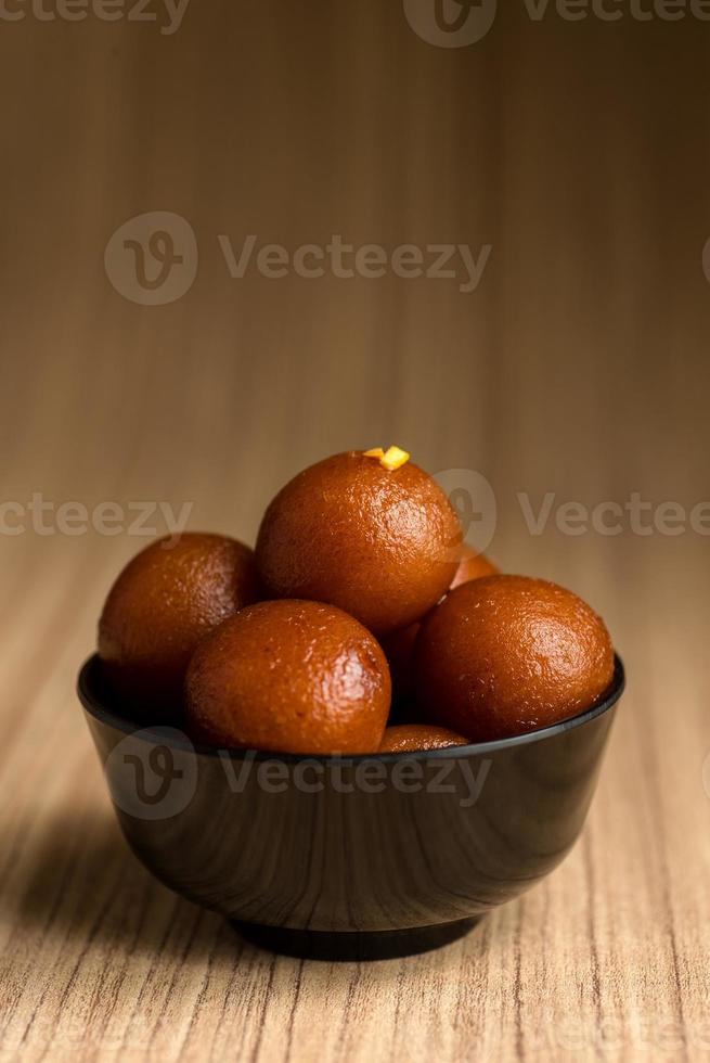 dessert indiano o piatto dolce gulab jamun in una ciotola su fondo di legno. foto