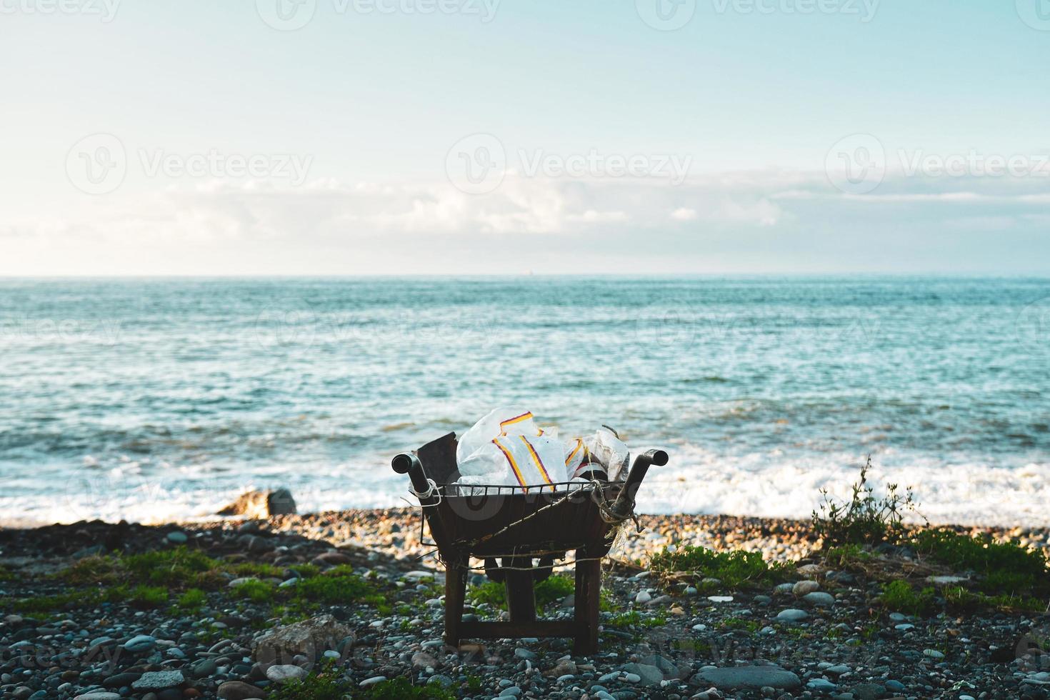 carriola piena di rifiuti di plastica stand sulla spiaggia con panorama sul mare. concetto di inquinamento in spiaggia, mare, oceano, proteggere e salvare il concetto di terra foto