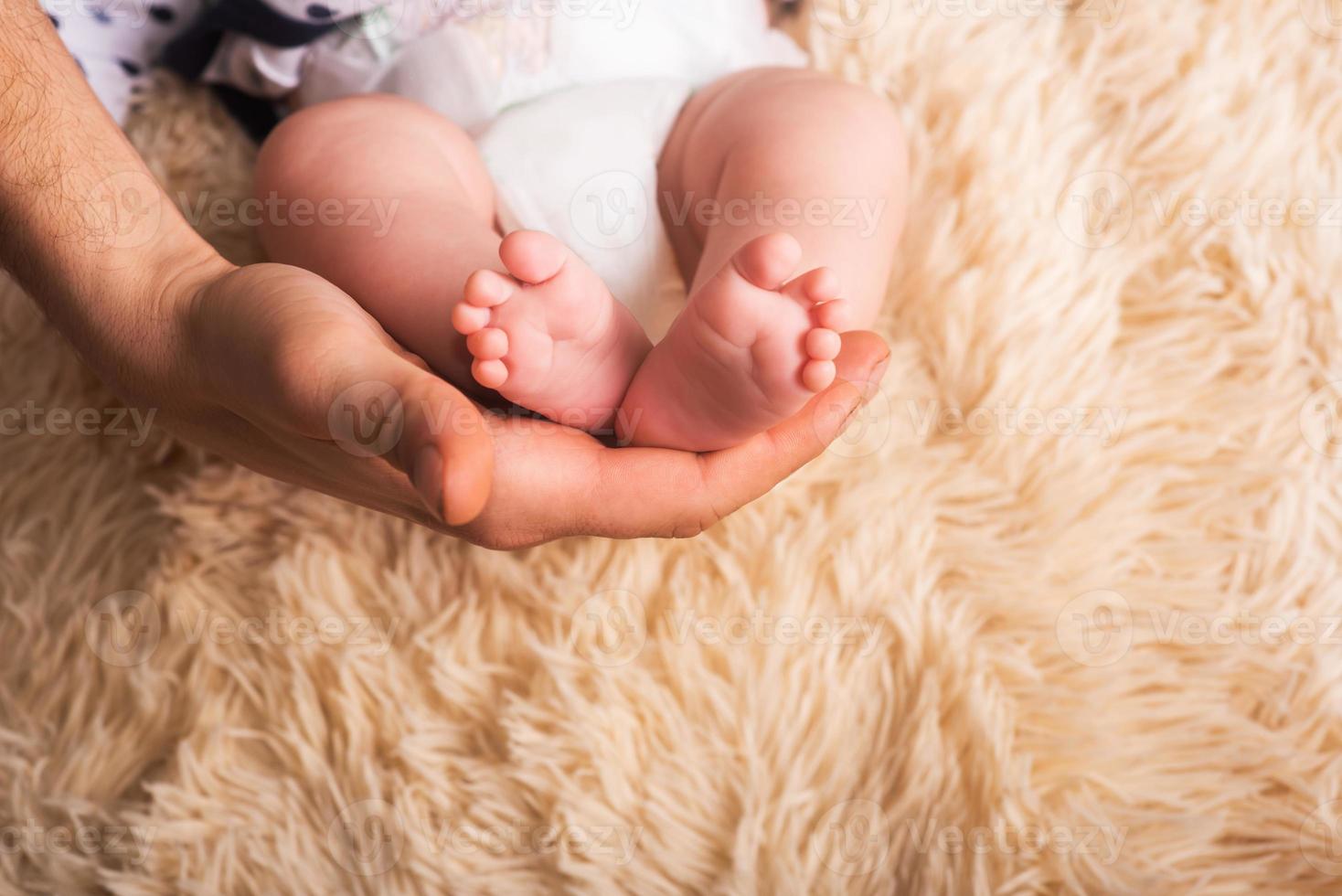 papà tiene tra le mani un bambino piccolo. piccole gambe di un neonato in grandi mani di papà. massaggio ai piedi del bambino foto