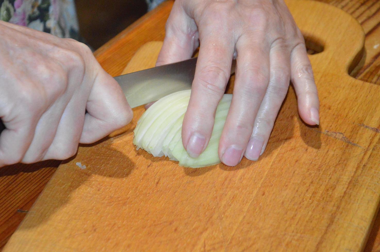affettare le cipolle con un coltello su un tagliere da cucina foto
