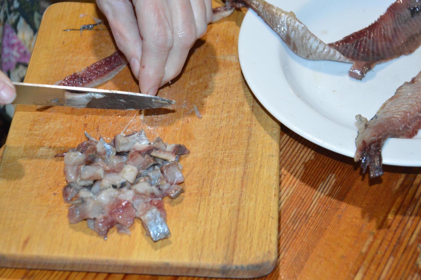 affettare le aringhe con un coltello su un tagliere da cucina foto