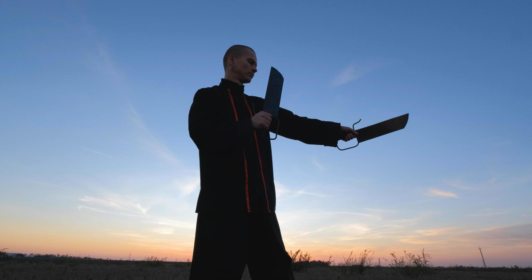 silhouette di un giovane combattente di kung fu maschio che si esercita da solo nei campi durante il tramonto foto