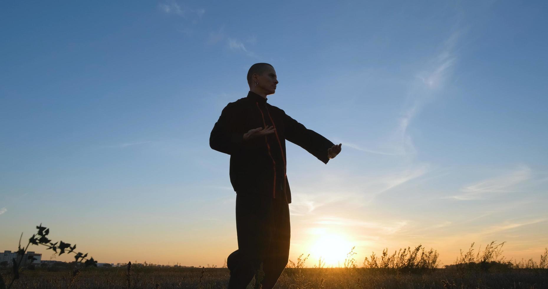 silhouette di un giovane combattente di kung fu maschio che si esercita da solo nei campi durante il tramonto foto