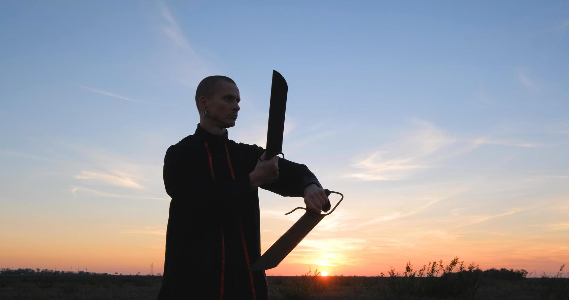 silhouette di un giovane combattente di kung fu maschio che si esercita da solo nei campi durante il tramonto foto