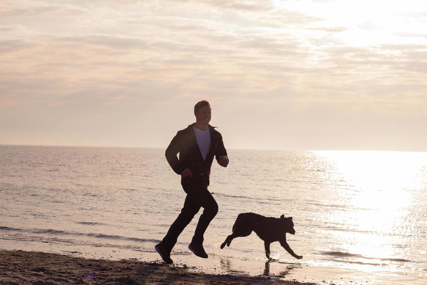 giovane che cammina sulla spiaggia mattutina con un cane nero foto