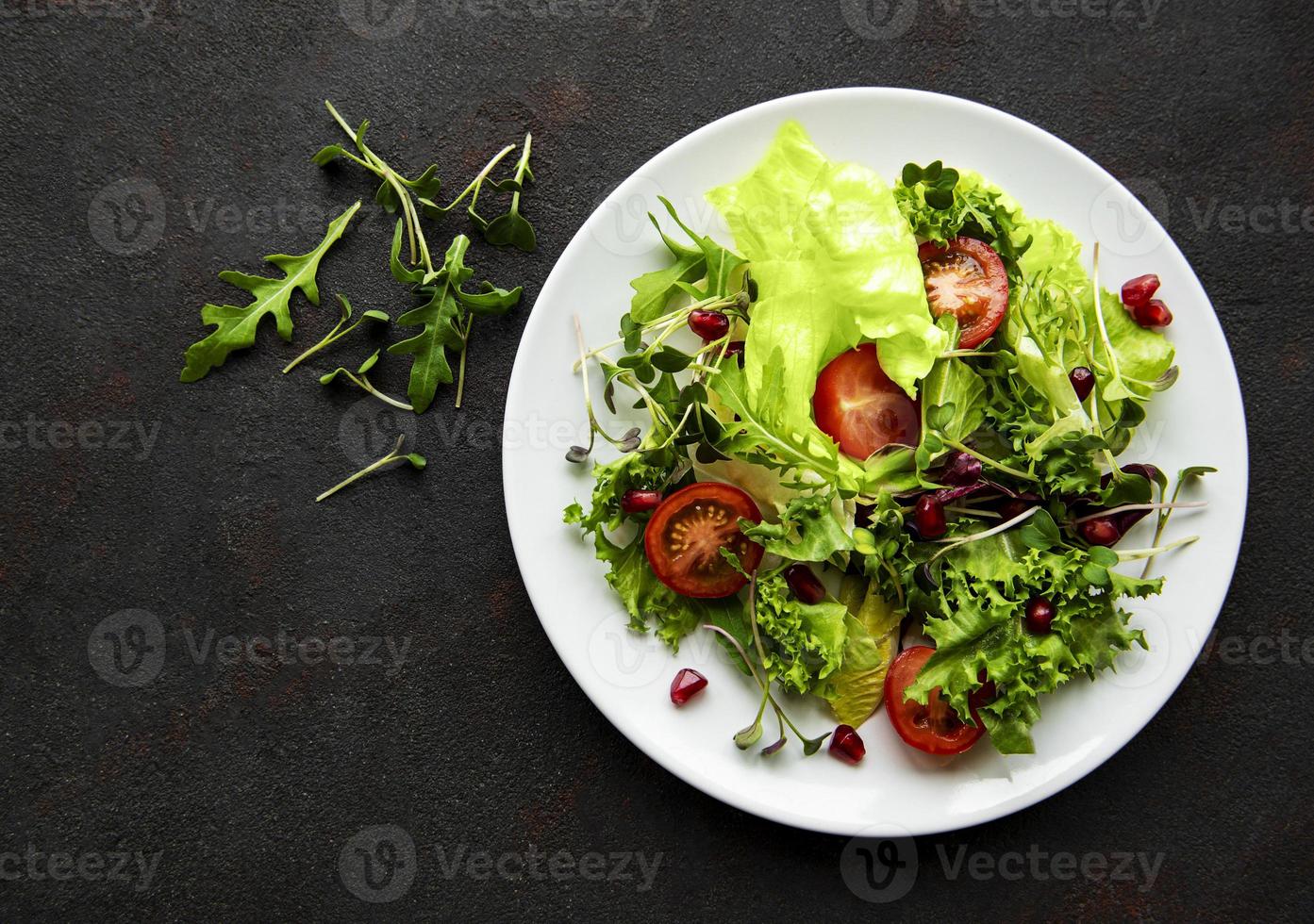 insalatiera mista verde fresca con pomodori e microgreens su sfondo di cemento nero. cibo sano, vista dall'alto. foto