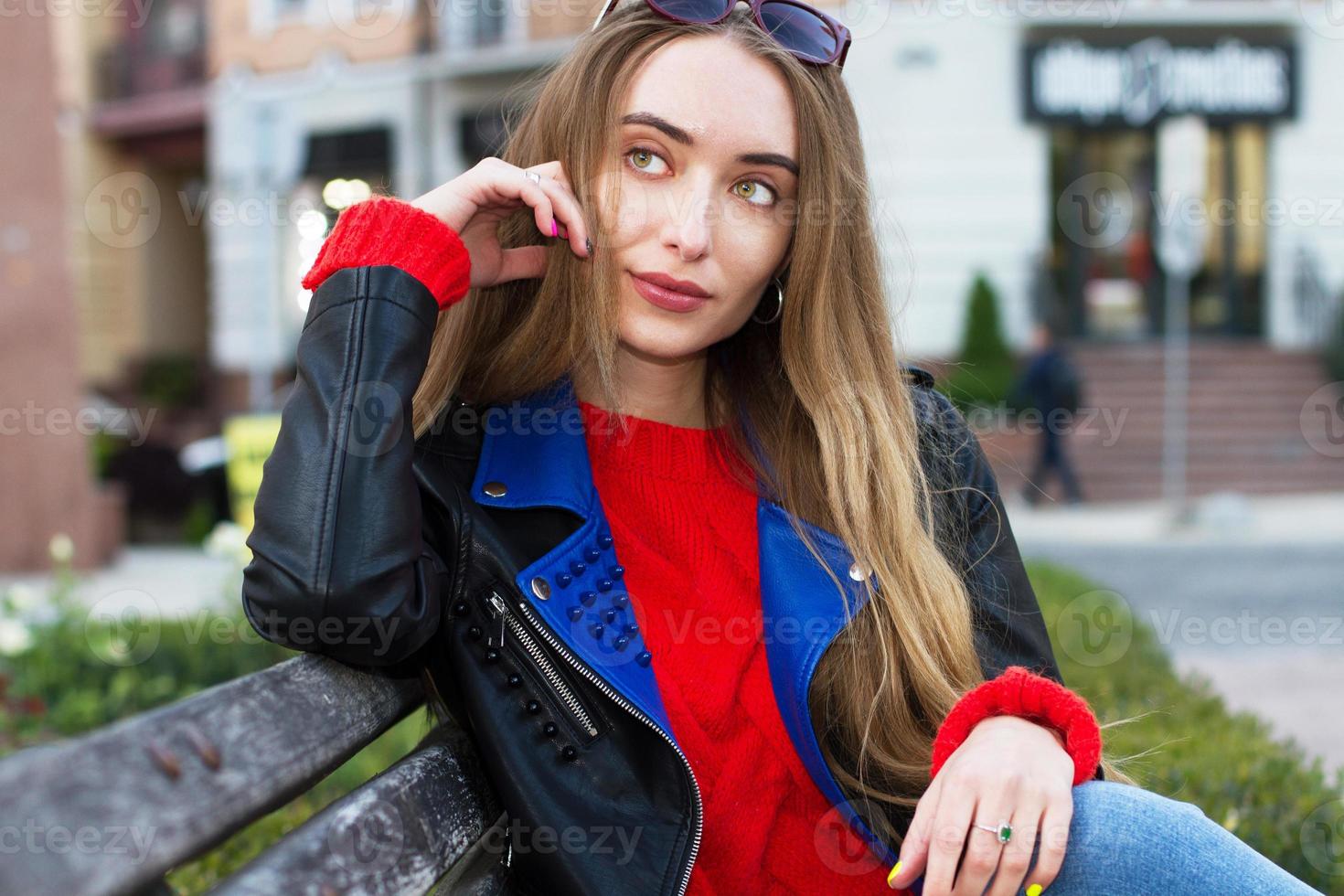 primo piano bella giovane donna bianca che indossa occhiali da sole, maglione elegante e giacca di pelle in posa per strada, bella donna sexy ed elegante sorriso su sfondo urbano, donne bianche in una grande città foto