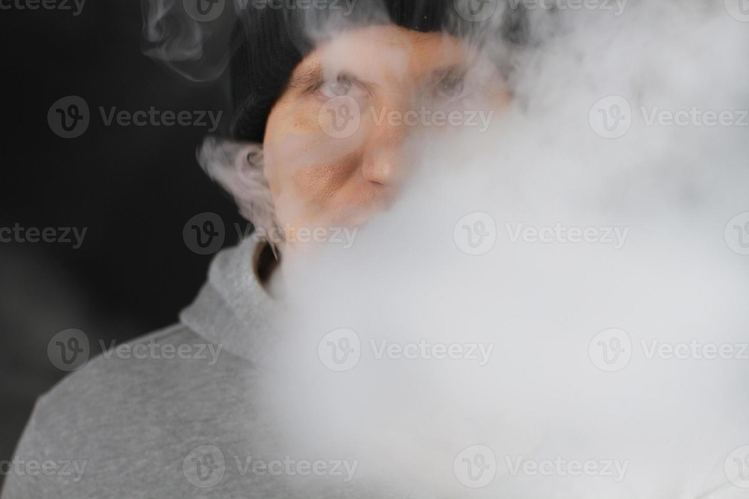 molto fumo bianco - il vaper esala una nuvola di fumo su sfondo scuro, l'uomo vape messa a fuoco selettiva foto