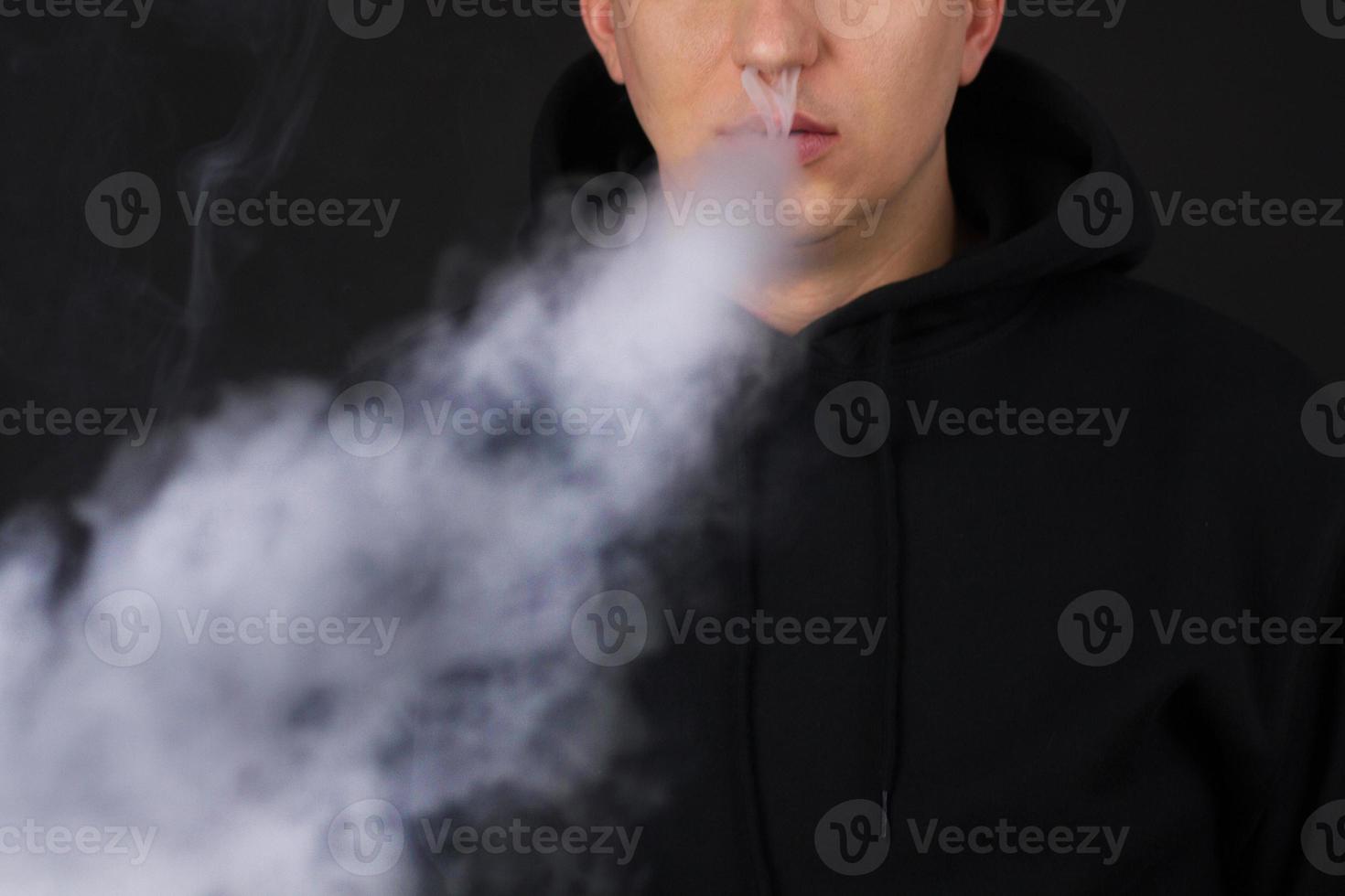 uomo irriconoscibile nella nuvola di fumo di vape. ragazzo che fuma sigaretta elettronica per smettere di fumare. vapore e concetto di fumo alternativo senza nicotina, copia spazio messa a fuoco selettiva foto