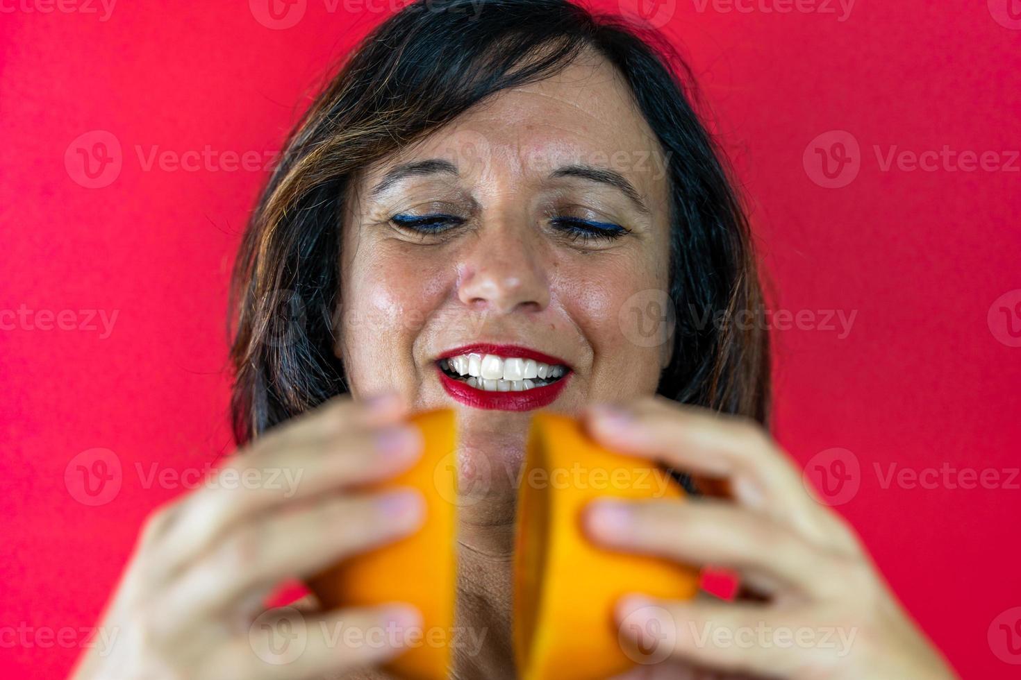 il ritratto di una donna di mezza età attraente tiene tra le mani due arance tagliate a metà foto