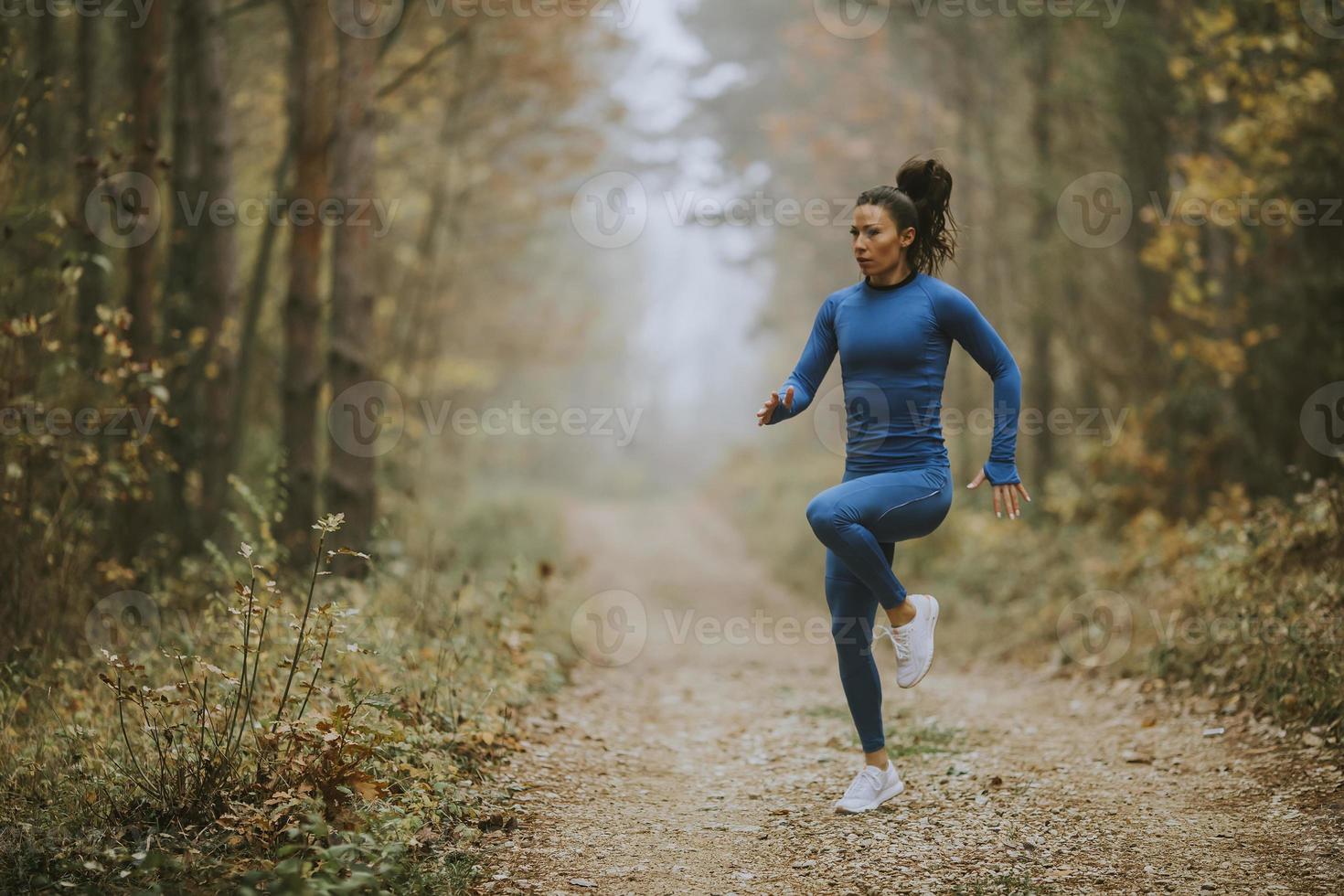 giovane donna che corre facendo esercizio sul sentiero nel bosco in autunno foto