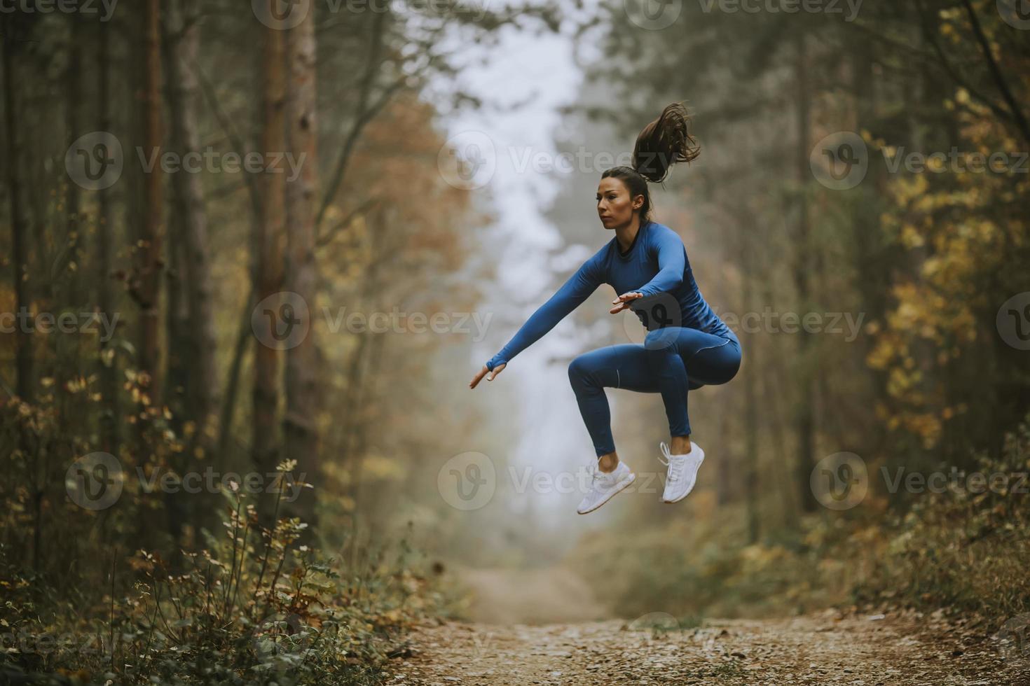 giovane donna che fa il salto in alto sul sentiero nel bosco in autunno foto