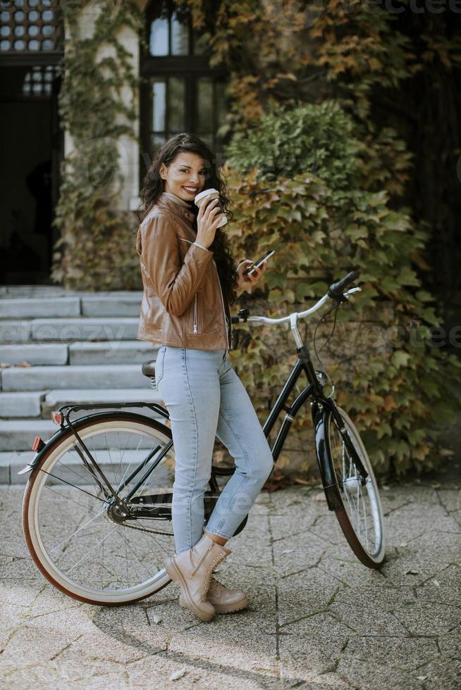 giovane donna con il cellulare beve caffè per andare in bicicletta il giorno d'autunno foto