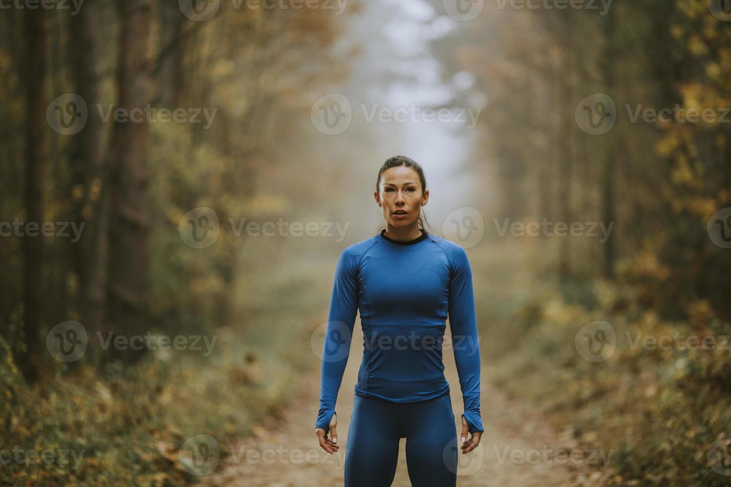 la giovane donna si prende una pausa durante l'esercizio all'aperto sul sentiero nel bosco in autunno foto