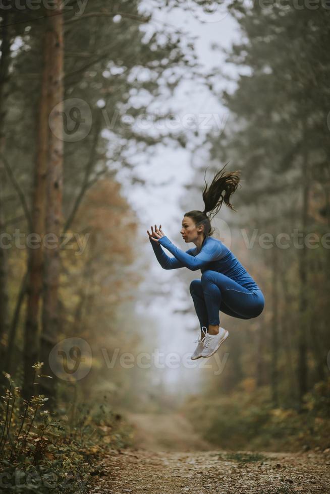 giovane donna che fa il salto in alto sul sentiero nel bosco in autunno foto