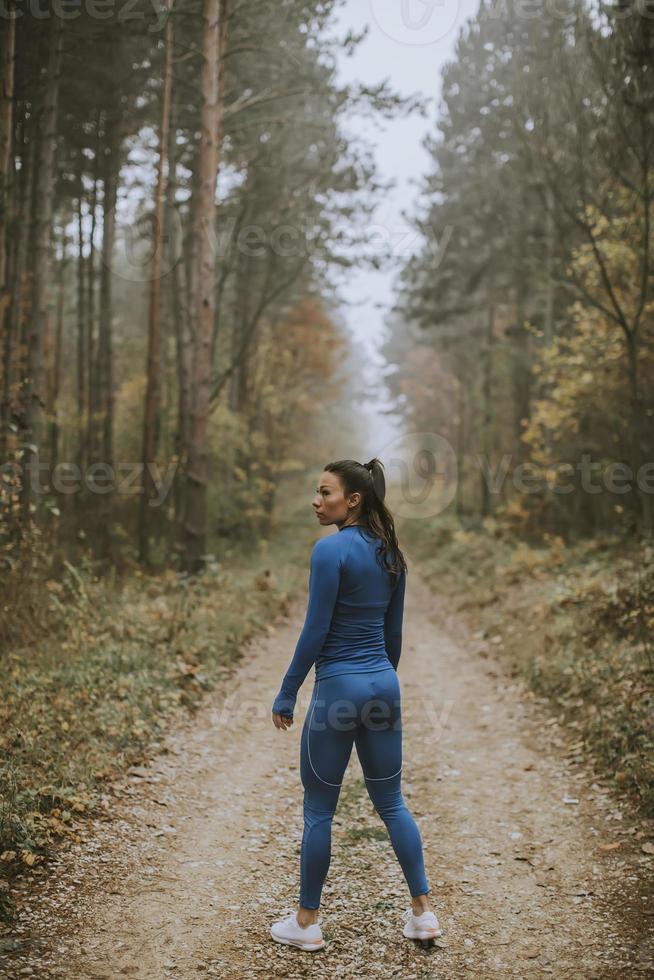 la giovane donna si prende una pausa durante l'esercizio all'aperto sul sentiero nel bosco in autunno foto