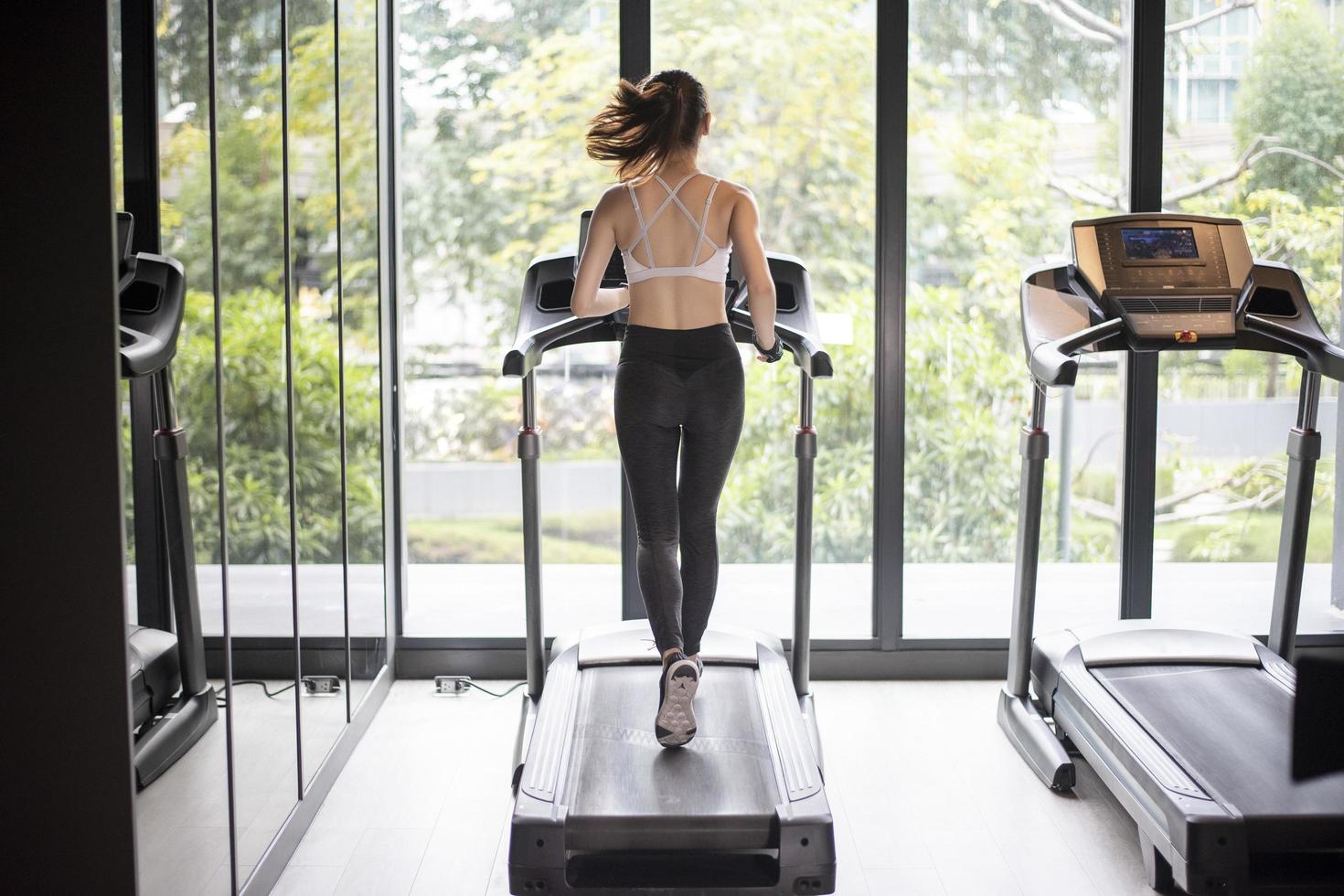 la bella donna asiatica di sport sta correndo sul tapis roulant in palestra foto