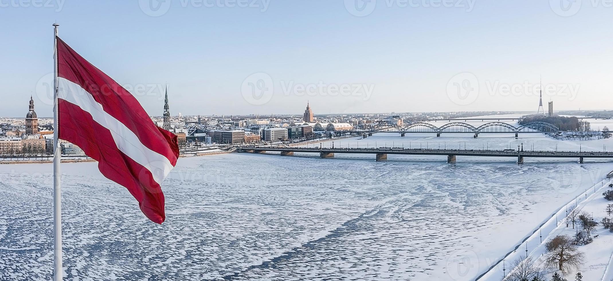 panorama della città di riga con una grande bandiera lettone in primo piano durante la soleggiata giornata invernale. foto