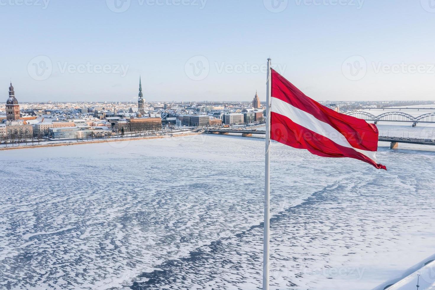 panorama della città di riga con una grande bandiera lettone in primo piano durante la soleggiata giornata invernale. foto