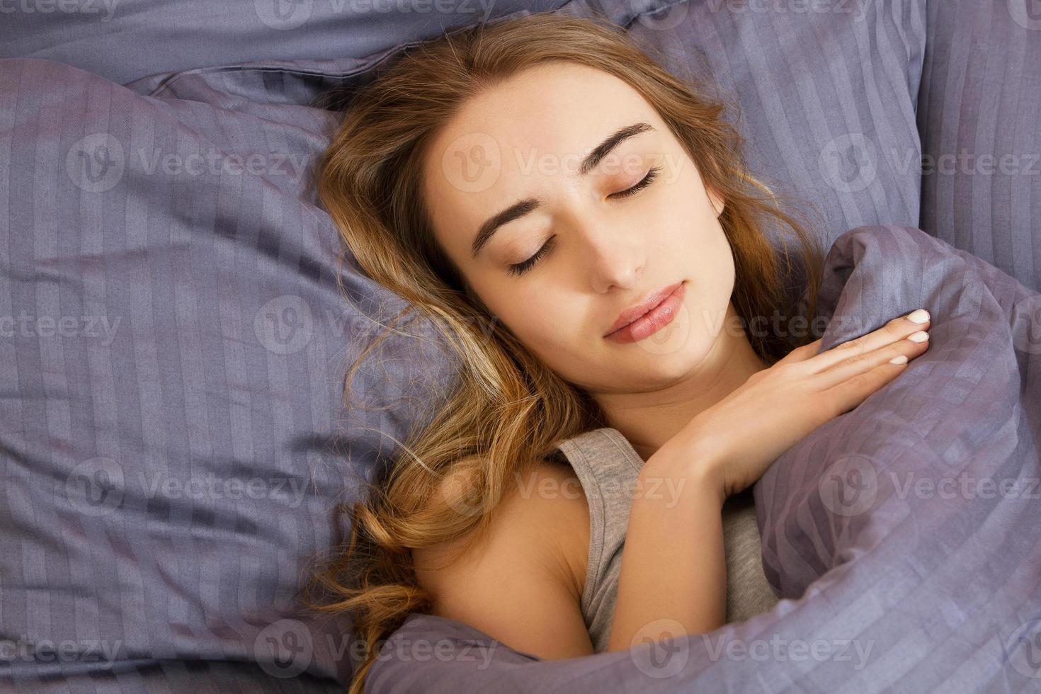 ritratto di bella giovane donna che dorme sdraiata a letto comodamente e beatamente - il sole splende dalla finestra sul suo viso foto