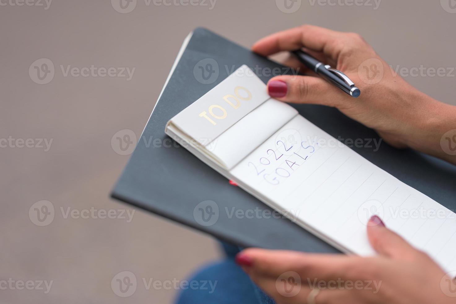 donna di colore con smalto rosso che scrive la risoluzione del suo nuovo anno in un taccuino con una penna nera foto