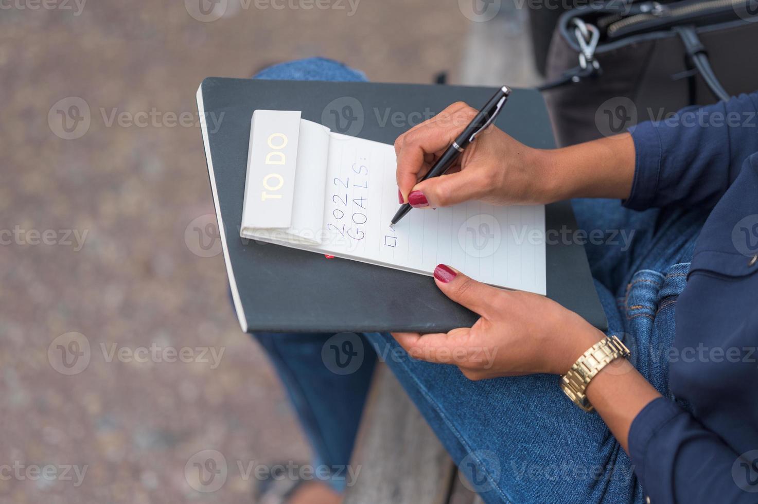 donna di colore con smalto rosso che scrive la risoluzione del suo nuovo anno in un taccuino con una penna nera foto