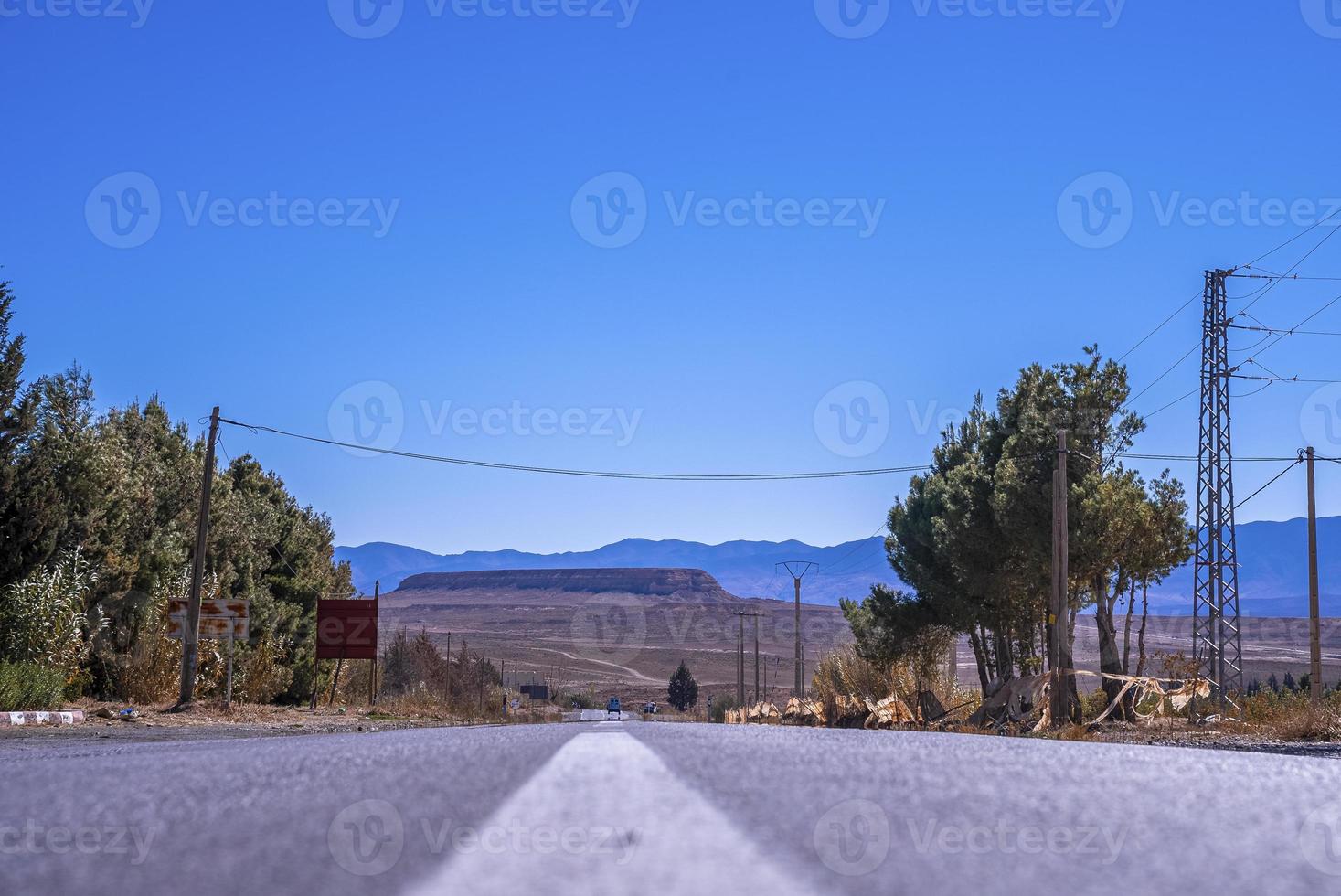 strada asfaltata diritta con marcatura di superficie bianca contro le montagne sullo sfondo foto