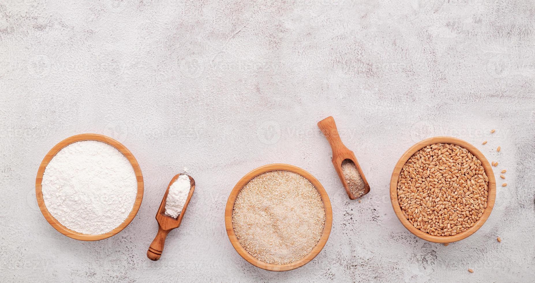 chicchi di grano, farina di grano marrone e farina di grano bianco in una ciotola di legno allestita su sfondo bianco di cemento. foto