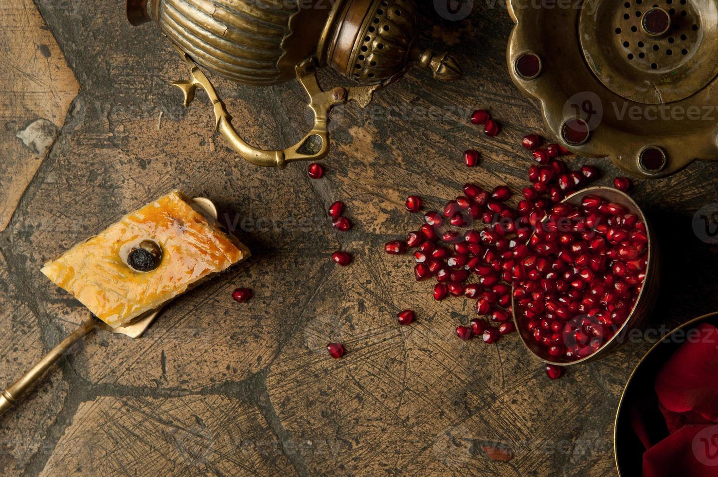 chicchi e semi di melograno con una brocca di rame su una vecchia pietra decorativa per lastricati. un'antica brocca di rame con un melograno e una torta su una vecchia piastrella foto