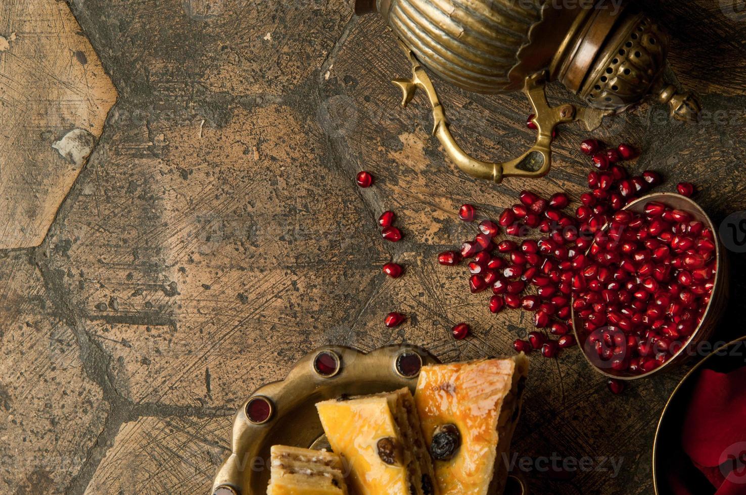 chicchi e semi di melograno con una brocca di rame su una vecchia pietra decorativa per lastricati. un'antica brocca di rame con un melograno e una torta su una vecchia piastrella foto