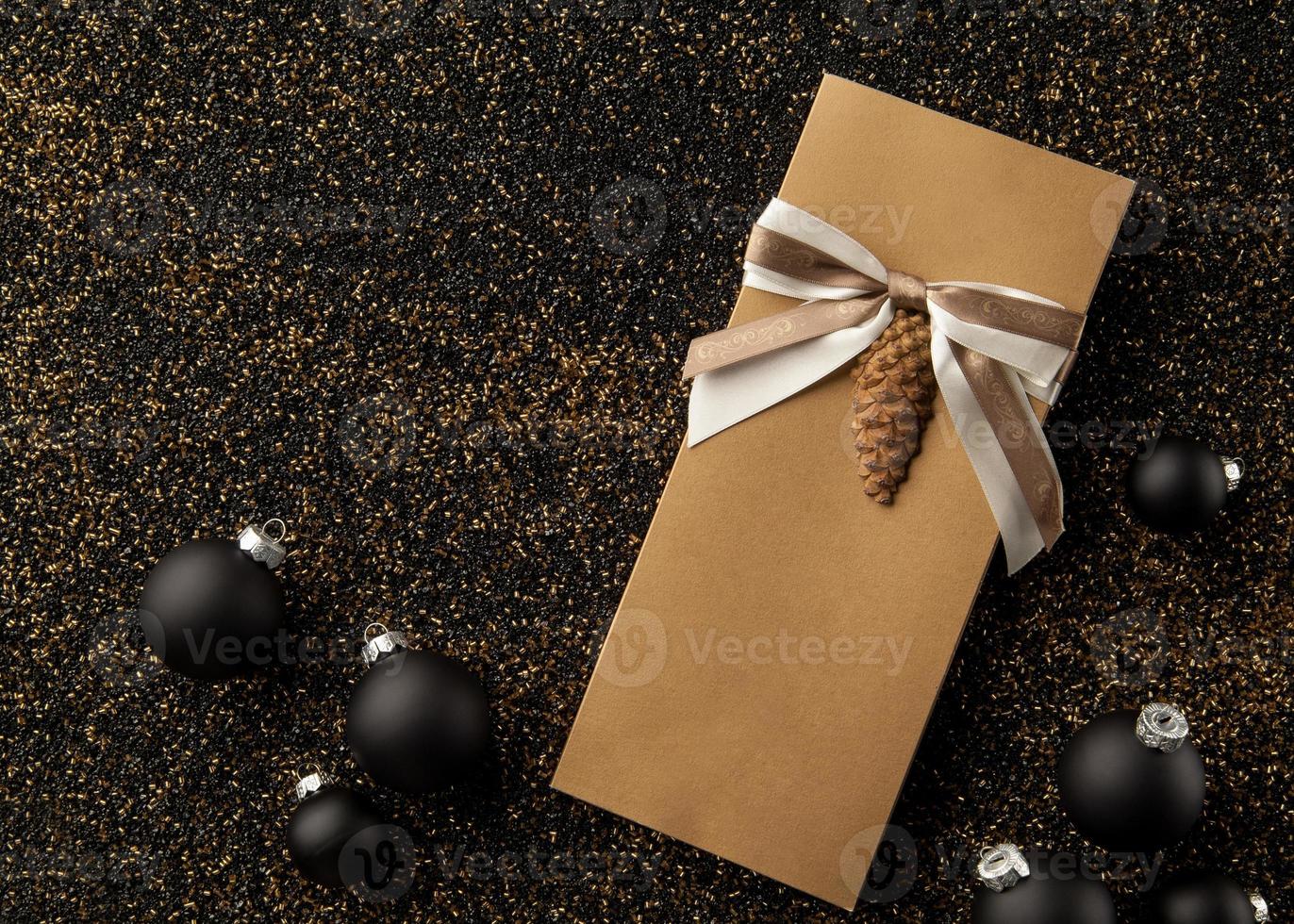 libretto regalo con decorazioni per l'albero di natale su fondo granuloso dorato. volantino con nastro su sfondo nero granuloso dorato foto