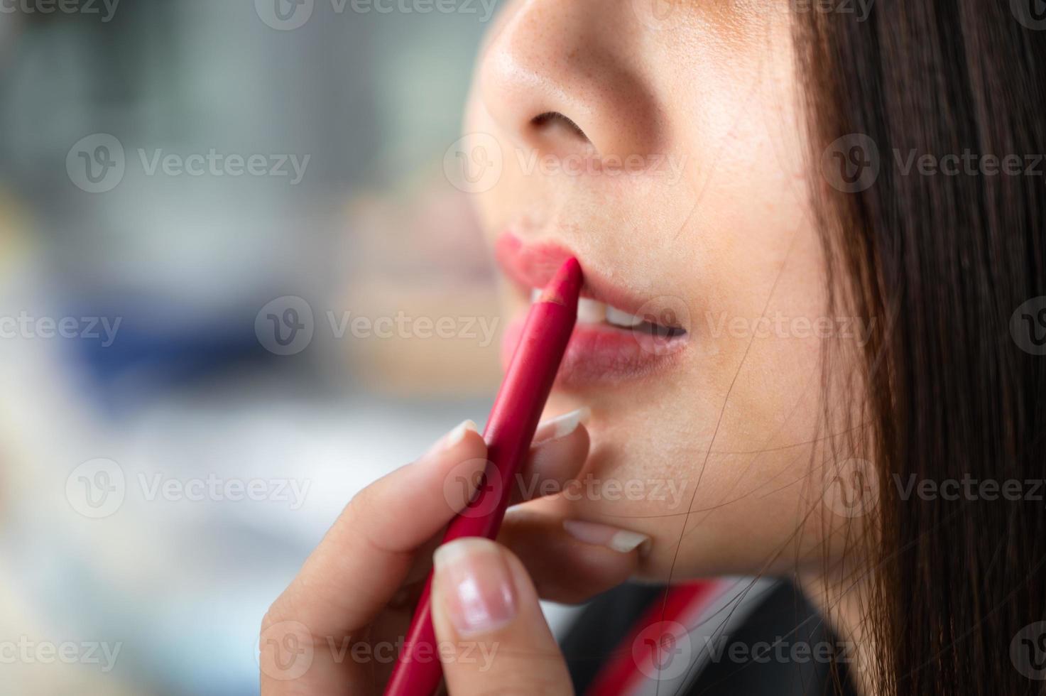 bella donna asiatica che applica la matita rossa del rossetto sulle sue labbra foto