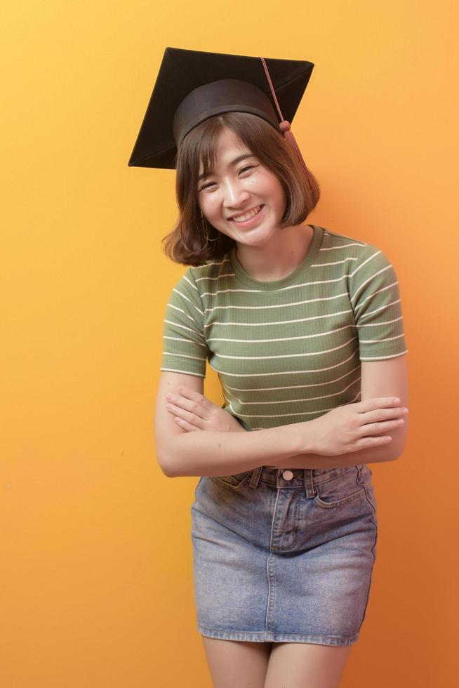 Ritratto di giovane studente asiatico che indossa il cappello di laurea su sfondo di studio. foto