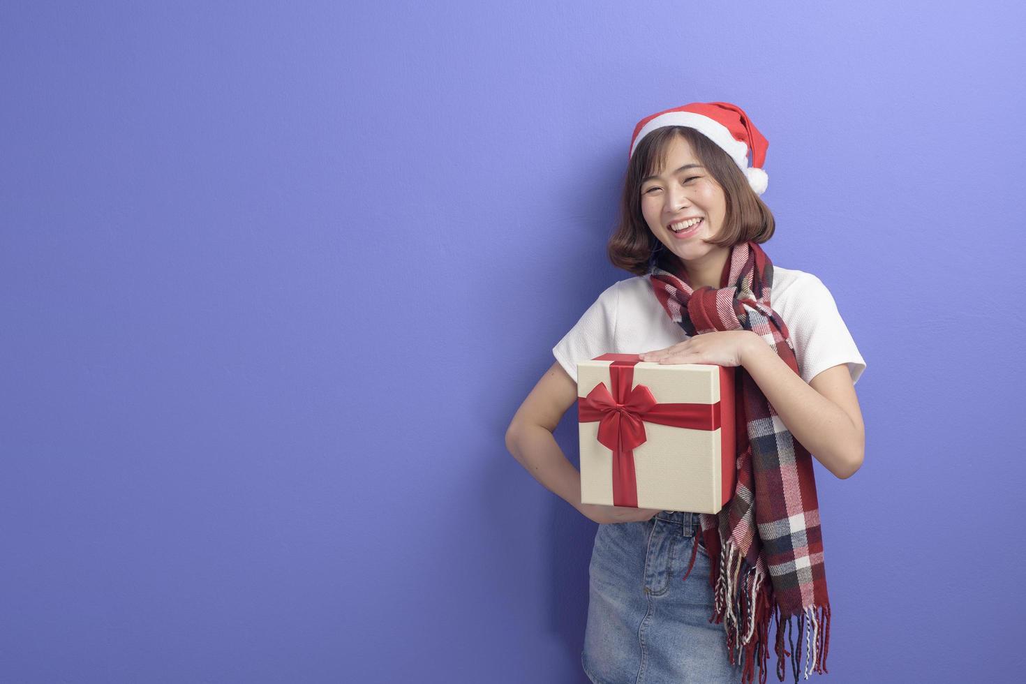 Ritratto di bella donna che indossa il cappello rosso di Babbo Natale che tiene una confezione regalo su sfondo per studio, concetto di Natale e Capodanno foto