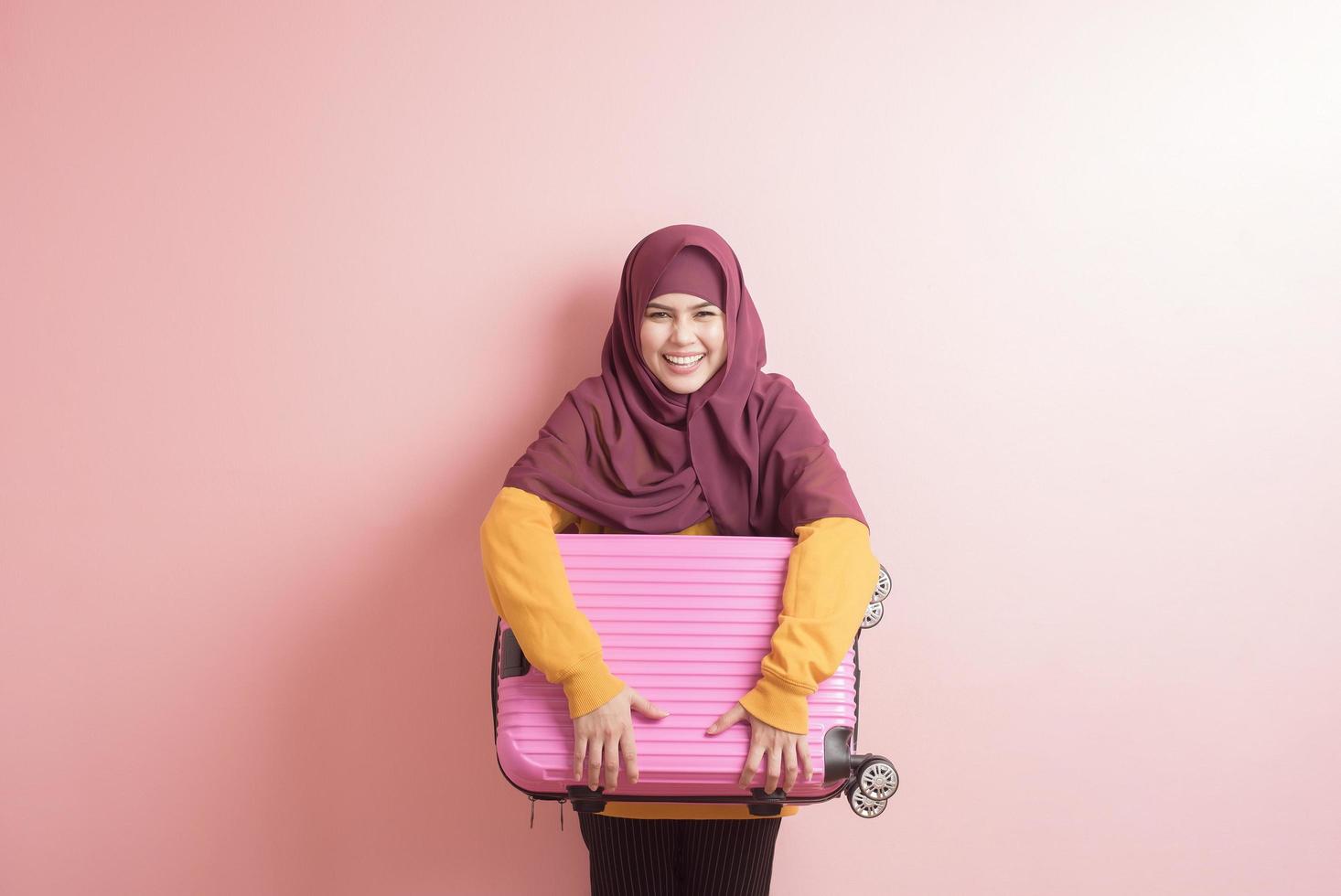 la donna musulmana con l'hijab sta tenendo i bagagli su sfondo rosa, concetto di viaggio della gente foto