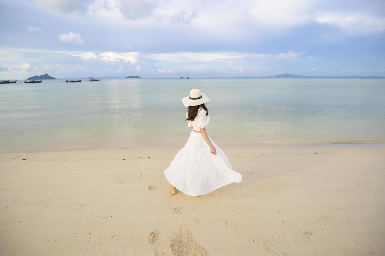 una bella donna felice in abito bianco che si gode e si rilassa sul concetto di spiaggia, estate e vacanze foto