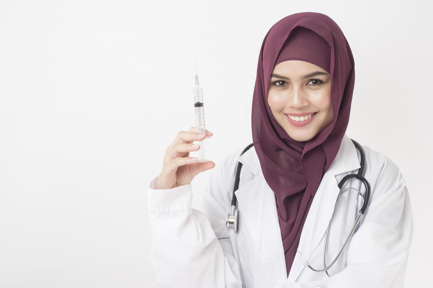 bella donna medico con hijab sta tenendo la siringa su sfondo bianco foto