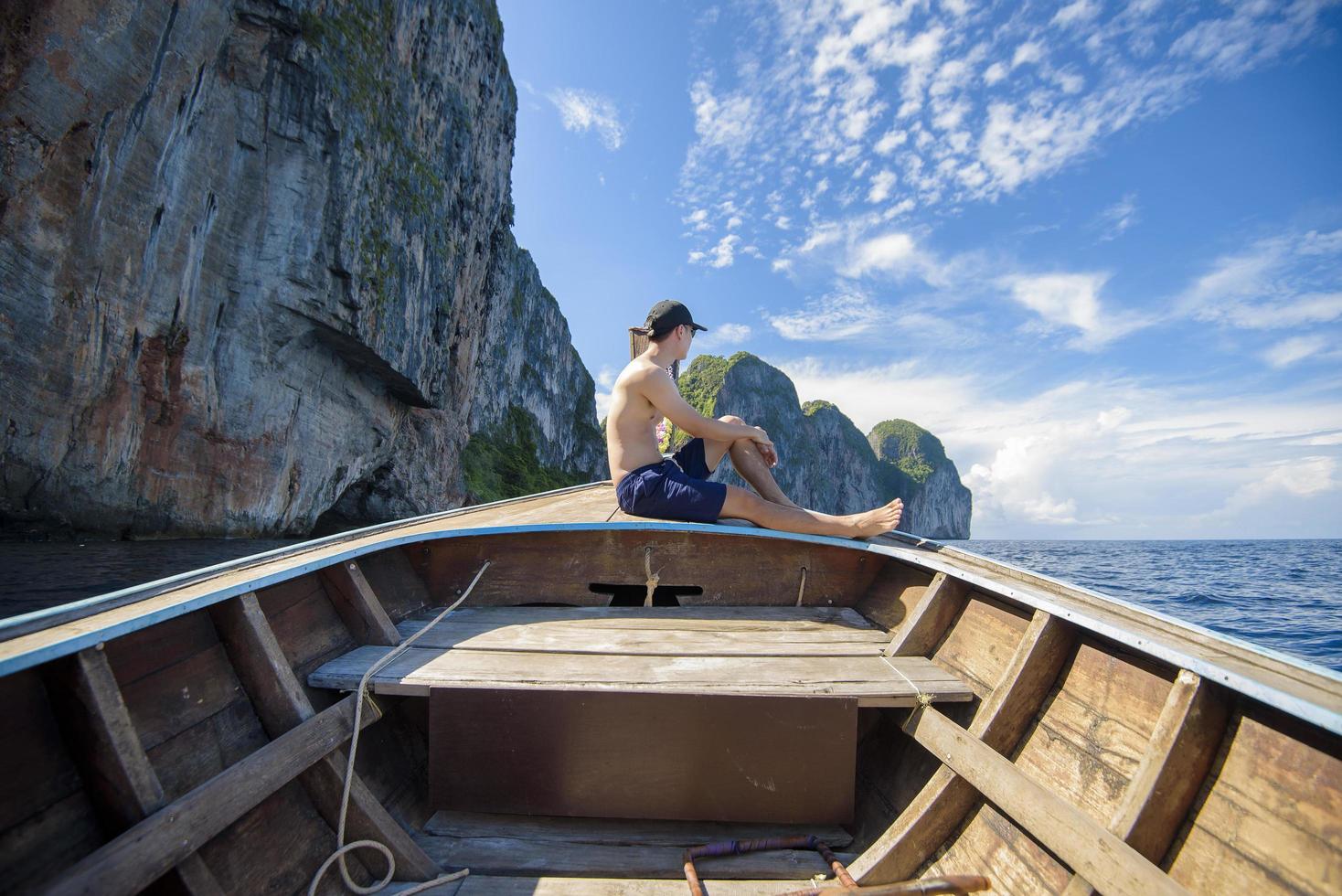 Vista dell'uomo in costume da bagno godendo sulla tradizionale barca tailandese a coda lunga sulla bellissima montagna e sull'oceano, isole phi phi, tailandia foto