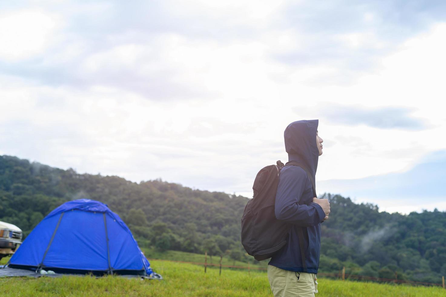 uomo di viaggio felice che si diverte e si rilassa vicino alla tenda del campo sulla bellissima montagna verde nella stagione delle piogge, clima tropicale. foto