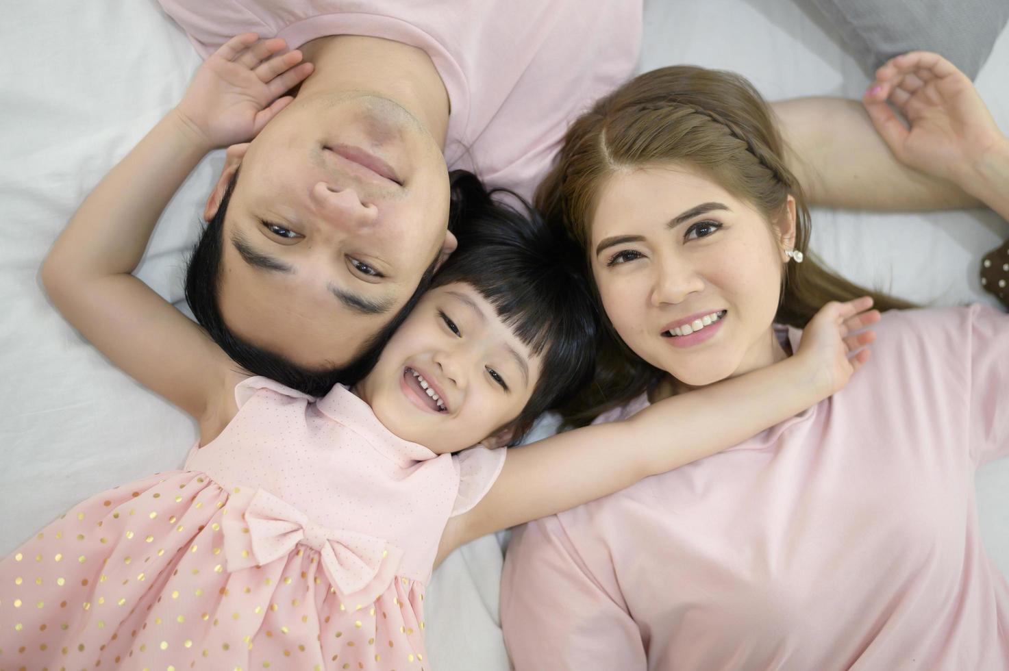 vista dall'alto di una famiglia asiatica felice che indossa un ritratto di camicia rosa sul letto bianco al coperto foto