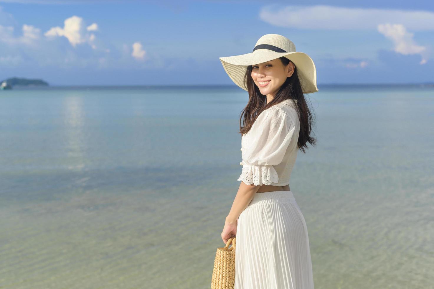 una bella donna felice in abito bianco che si gode e si rilassa sul concetto di spiaggia, estate e vacanze foto