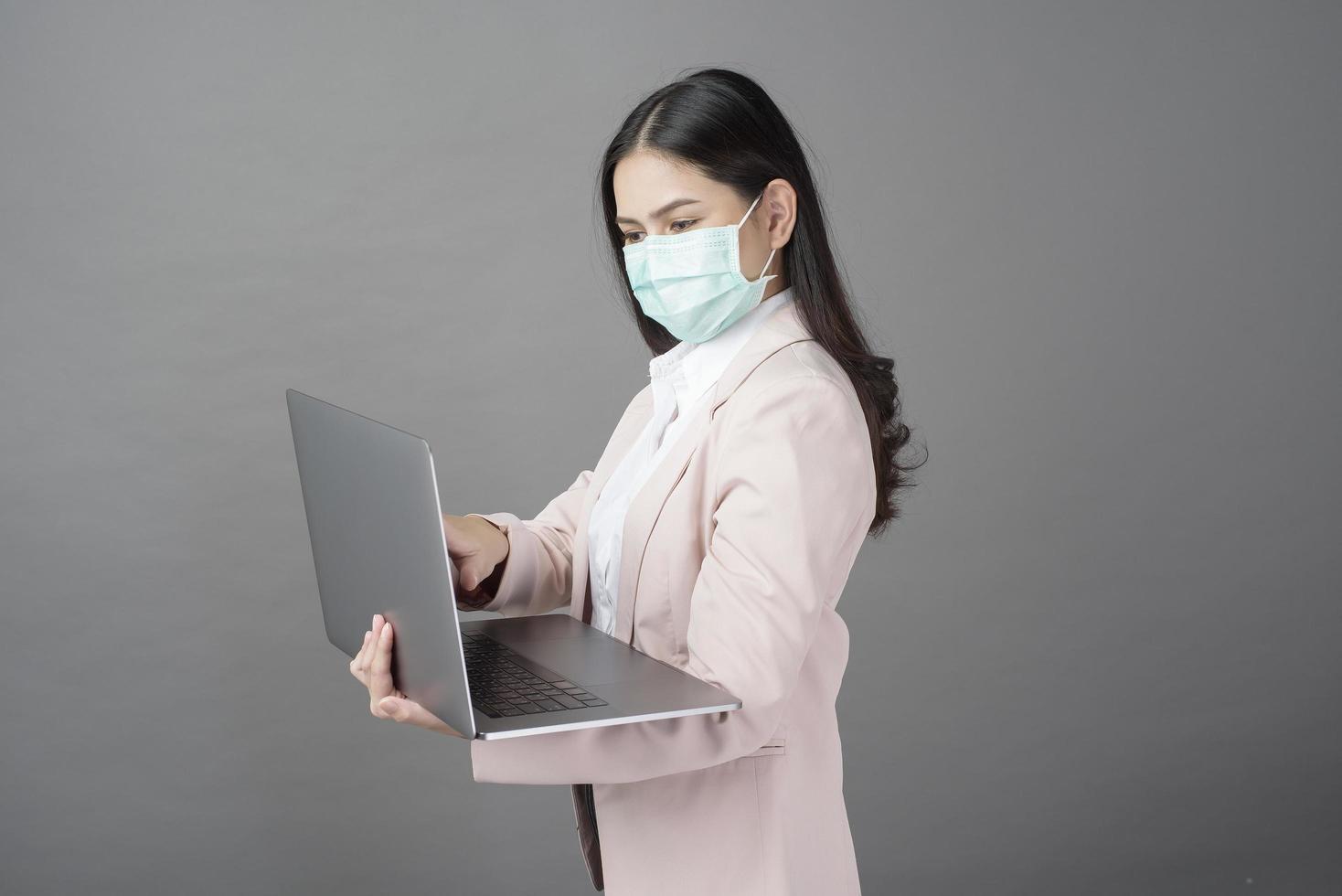 donna d'affari con maschera chirurgica tiene in mano un computer portatile foto