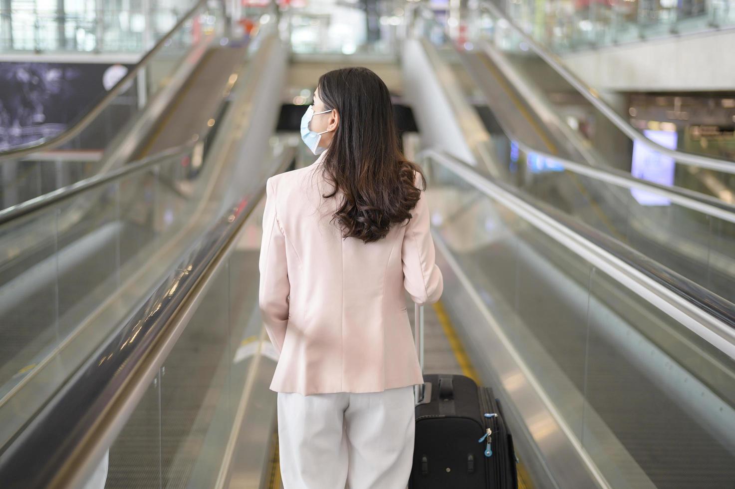 una donna d'affari indossa una maschera protettiva nell'aeroporto internazionale, viaggia sotto la pandemia covid-19, viaggi di sicurezza, protocollo di allontanamento sociale, nuovo concetto di viaggio normale foto