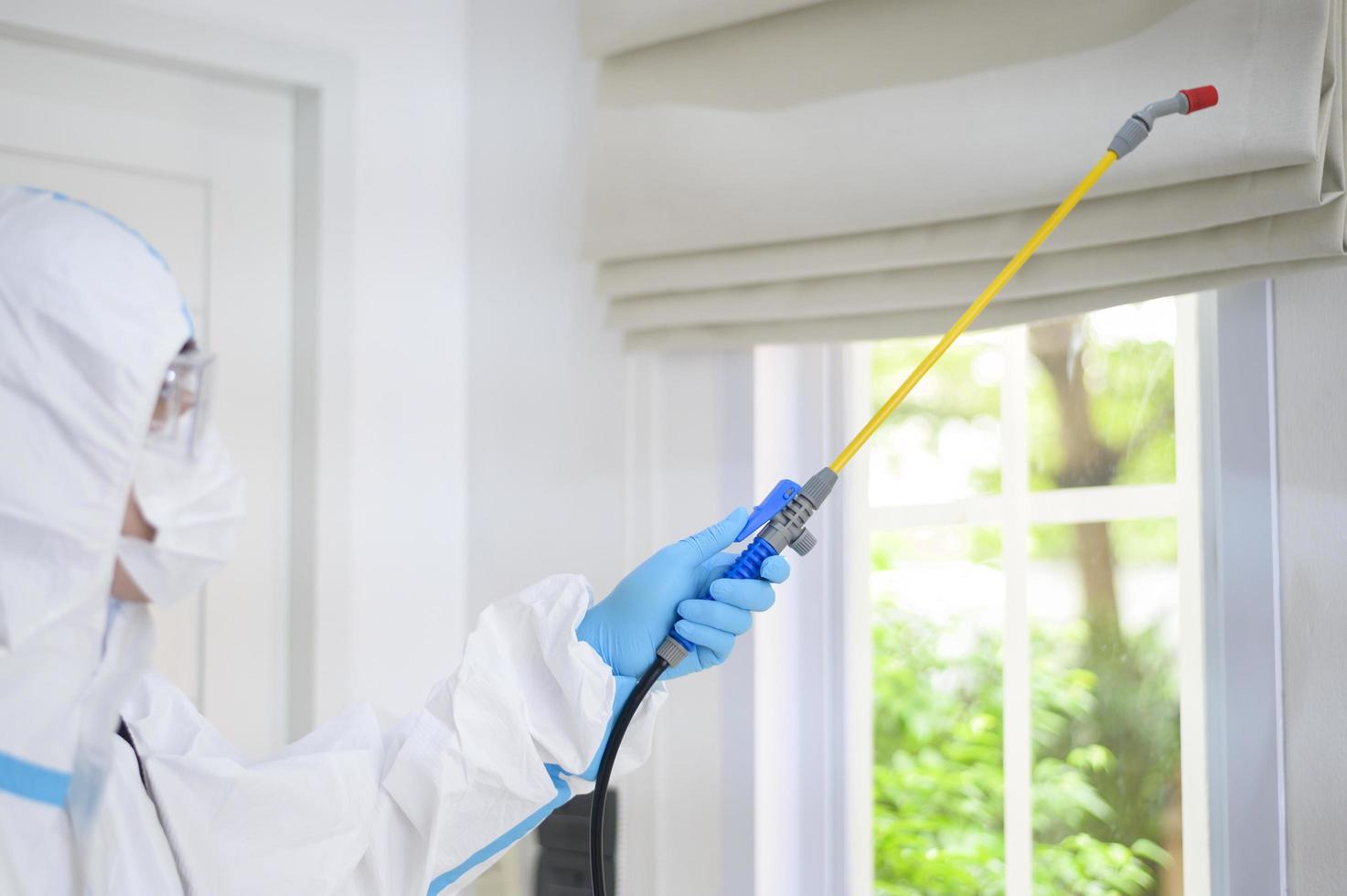 uno staff medico in tuta dpi sta usando spray disinfettante in soggiorno, protezione covid-19, concetto di disinfezione. foto