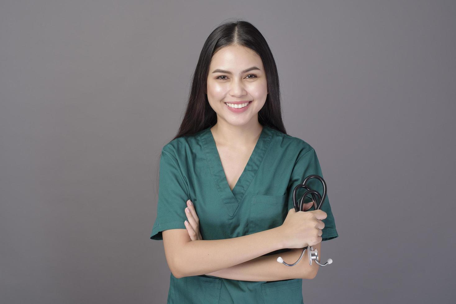 una dottoressa che indossa uno scrub verde e uno stetoscopio è su sfondo grigio studio foto