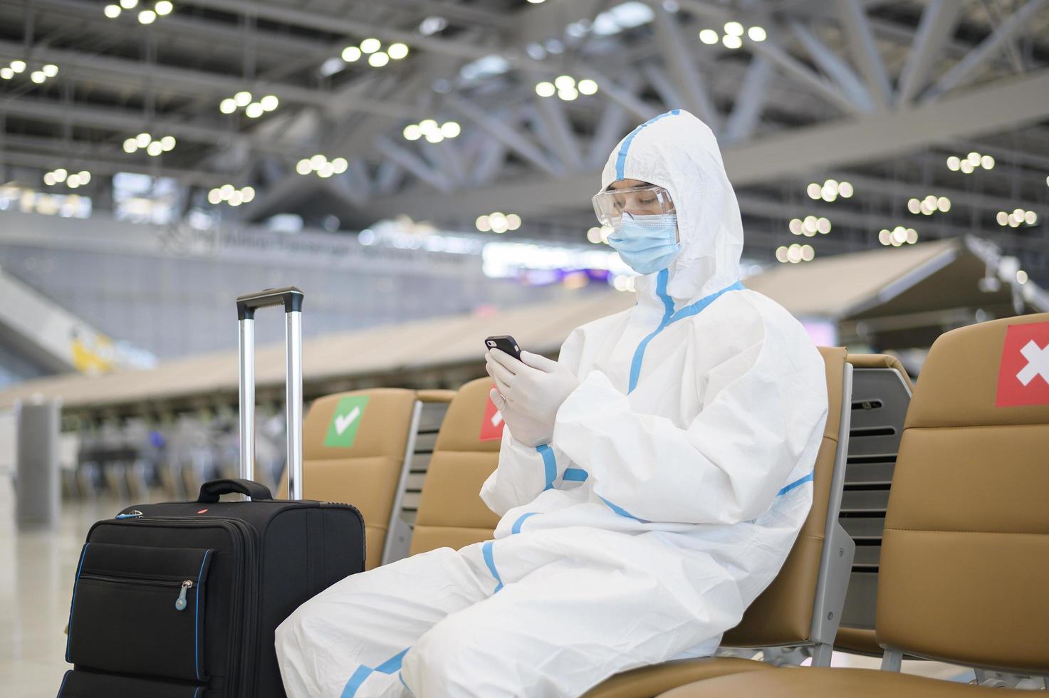 un uomo asiatico indossa una tuta dpi in aeroporto internazionale, viaggi di sicurezza, protezione covid-19, concetto di allontanamento sociale foto