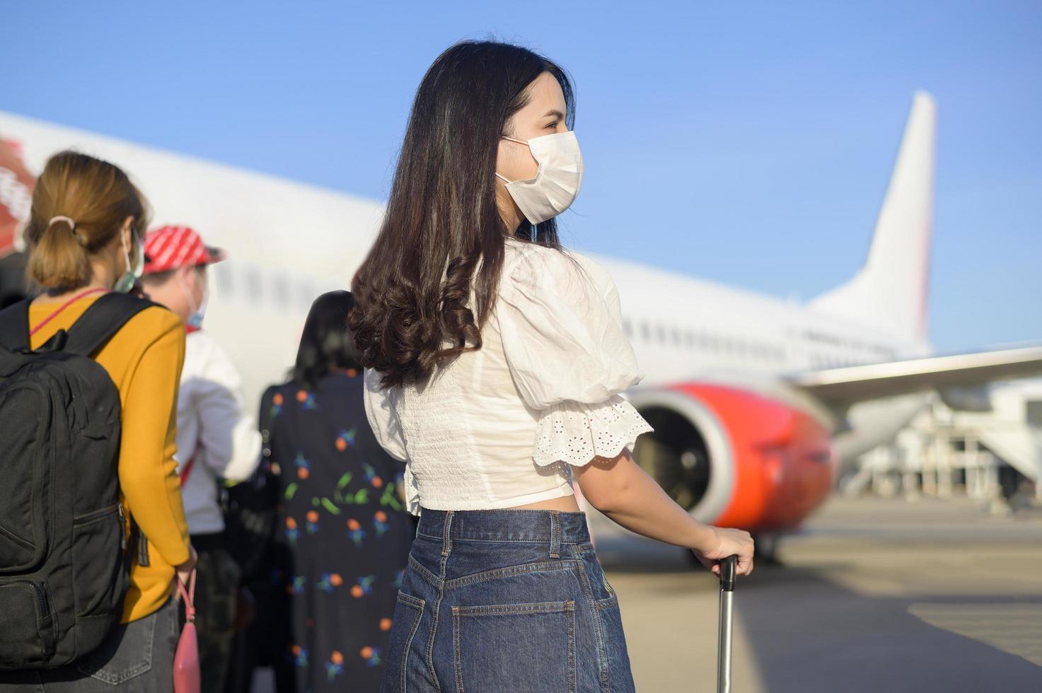 una giovane donna che indossa una maschera protettiva che sale in aereo e pronta a decollare, viaggiare sotto la pandemia di covid-19, viaggi di sicurezza, protocollo di allontanamento sociale, nuovo concetto di viaggio normale foto